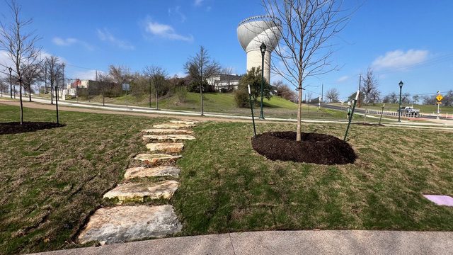 Stone pathway leads to a modern sculpture on a grassy hill under a clear sky.